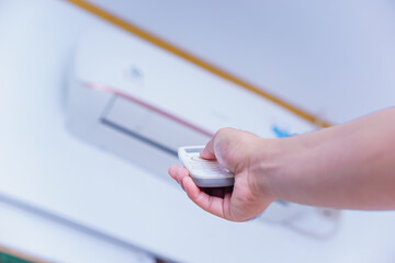 A person using a remote control to adjust an air conditioning unit mounted on the wall.