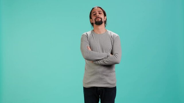 Grumpy man with sulking facial expression crossing arms, feeling annoyed, isolated over studio background. Portrait of irate person in bad mood feeling frustrated after argument, camera A