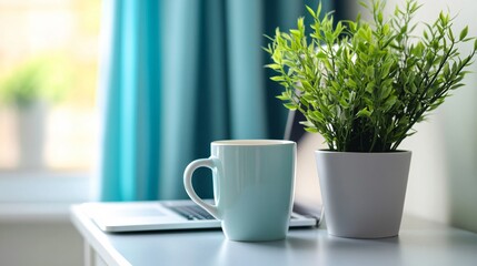 A blue mug and a potted plant on a white table next to a laptop computer.