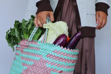 Closeup photo of a woman's hand carrying a shopping bag filled with fresh vegetables.