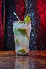 Vaso grande de limonada con rodajas de limón, hojas de menta y bombilla de metal, sobre mesa de madera rústica. Fondo natural