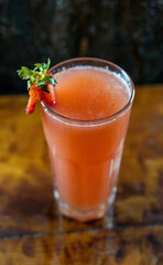 Vaso de jugo natural de frutilla con decoración de frutilla y hojas de menta, sobre mesa de madera rústica. Fondo cálido y natural