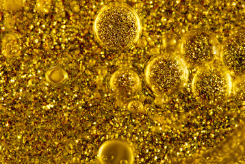 Close-up of golden glitter particles suspended in oil bubbles, creating a vibrant abstract texture.