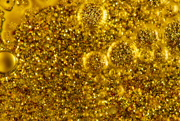 Close-up of golden glitter particles suspended in oil bubbles, creating a vibrant abstract texture.