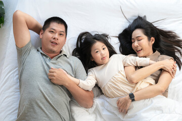 Obraz premium A joyful mother and daughter laughing together while lying on a bed. The playful moment showcases their strong bond and happiness in a comfortable home setting, surrounded by natural decor.