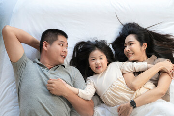 A joyful mother and daughter laughing together while lying on a bed. The playful moment showcases their strong bond and happiness in a comfortable home setting, surrounded by natural decor.