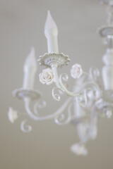 A beautiful white chandelier with three candles and three white roses. The candles are lit, creating a warm and inviting atmosphere. The roses are delicately placed on the chandelier