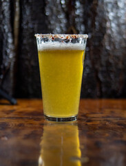 Vaso de michelada con cerveza y borde cubierto de ají merkén, sobre una mesa. Bebida refrescante...