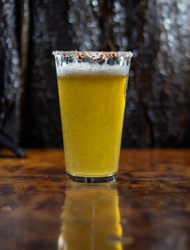 Vaso de michelada con cerveza y borde cubierto de aj&iacute; merk&eacute;n, sobre una mesa. Bebida refrescante con un toque picante y c&iacute;trico