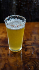 Vaso de michelada con cerveza y borde cubierto de ají merkén, sobre una mesa. Bebida refrescante con un toque picante y cítrico
