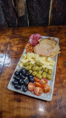 Tabla de cóctel con aceitunas, maní, jamón, tomate cherry, papas fritas y queso, ideal para compartir. Presentación rústica y apetitosa