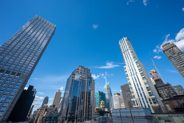 Obraz premium Stunning rooftop views of New York City’s skyline, featuring iconic skyscrapers under a clear blue sky. The crisp architecture contrasts against the vivid urban landscape, offering a classic perspecti