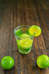 Organic cold refreshing lemonade drink or cocktail made of sparkling water, lime slices and fresh green mint leaves served in tall drinking glass with ice cubes on white wooden table with copy space