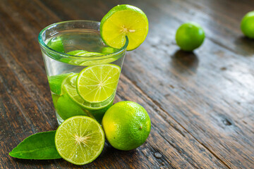 Organic cold refreshing lemonade drink or cocktail made of sparkling water, lime slices and fresh green mint leaves served in tall drinking glass with ice cubes on white wooden table with copy space