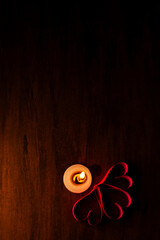 Candle surrounded by red paper hearts on dark background. Space for text. Background, romantic concept, poster, design for your project. Vertical