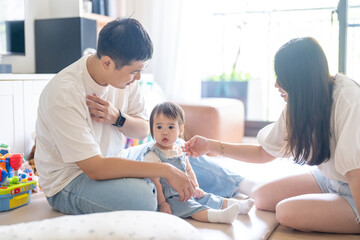 Obraz premium A 1 year old Taiwanese girl spending time playing happily with her parents, a man and woman in their 20s, in a room of a high rise apartment in Taichung City, Taiwan.