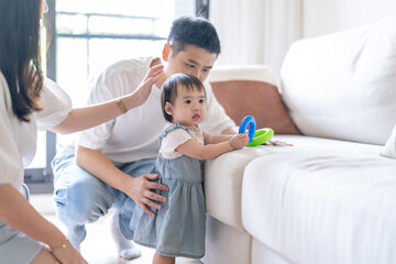 Obraz premium A 1 year old Taiwanese girl spending time playing happily with her parents, a man and woman in their 20s, in a room of a high rise apartment in Taichung City, Taiwan.