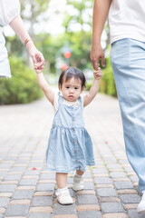 Fototapeta premium A 1 year old Taiwanese girl walking hand in hand with her parents, a man and woman in their 20s, on a hot sunny day in the streets of Taichung City, Taiwan, in September.