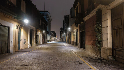 Calle estilo virreinal nocturna  empedrada con iluminación de faroles cálidas