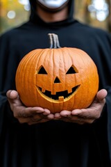 Halloween Jack o  Lantern Held By Person In Dark Cape And Mask