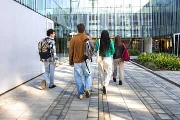 Back view of university students walking to class arriving at university building. Group of people...