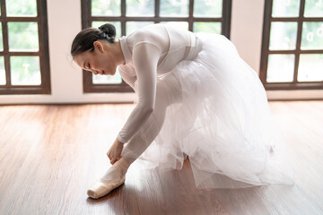 Ballerina in ballet shoes. Asian girl tying ribbons of toe shoes. ballet dancer preparing and wearing ballet shoes in dance studio prepares for a rehearsal.