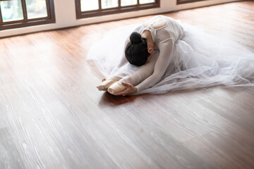 Asian girl ballet dancer gymnastic exercises in studio for body flexibility Ballerina training stretches her leg and prepares for performance practice routine.