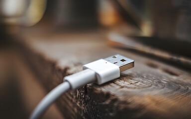 A close-up photo of Close up USB cable plug isolated on white background. The background is blurred, revealing a rustic setting. 