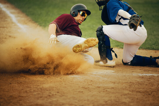Baseball player sliding into home plate evading catcher's tag with cleats kicking up dirt - Powered by Adobe