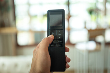 Human hand is turning-on air conditioner by pressing the button on remote control. Home appliance and interior object, close-up and selective focus.