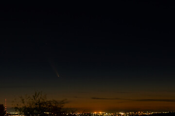 Fototapeta premium The periodic comet Tsuchinshan Atlas C 2023 A3 captured in the night sky above a city horizon.