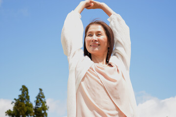 青空の下でバンザイをする笑顔の女性