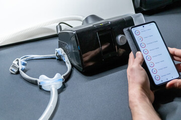 Male European with cpap machine checking therapy analysis via smartphone app or medical app for e-health check and health report via mobile device for health analysis innovative sleep apnea mask apps