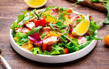 Fresh salad with canned tuna, tomatoes, onion, corn, paprika, lettuce and arugula. Rustic table background, top view
