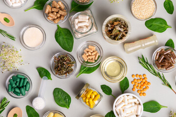 Many homeopathic meds, pills, tablets, herbs, green leaves and other natural organic products in a beautiful composition on a light grey background, top view. Homeopathy and alternative medicine.