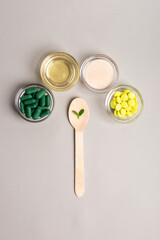 Homeopathic medicine. Homeopathic pills in a glass bowls, green leaves on wooden spoons from above on a light grey background. Alternative medicines top view.