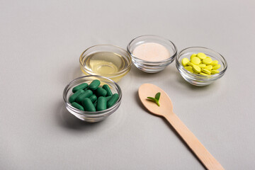 Homeopathic medicine. Homeopathic pills in a glass bowls, green leaves on wooden spoons from above on a light grey background. Alternative medicines top view.