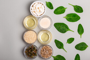 Homeopathic medicine. White homeopathic pills in a white ceramic plate and green leaves, herbs and natural products in glass bowls from above on a light grey background. Alternative medicines top view