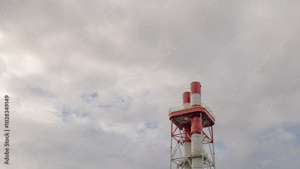 Wall mural chimneys against a cloudy sky. two tall red and white chimneys stand against a cloudy sky