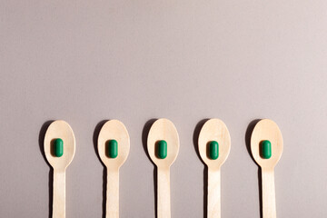 Wooden spoons with green tablets from above on a grey background. Dietary supplements and vitamins.