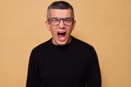 Caucasian guy feeling nervous and upset while shouting in frustration with his jaw clenched and voice raised showcasing aggression isolated over beige background