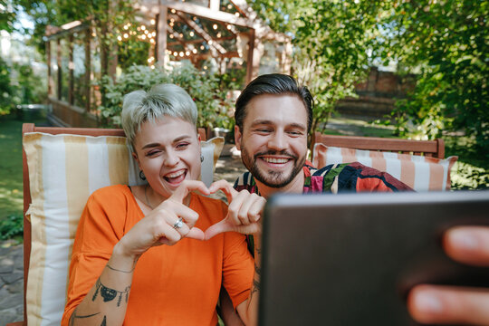 Happy man taking selfie with friend making heart shape with hands