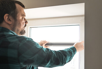 Man installs roller blinds. Handyman mesures window to fix it.