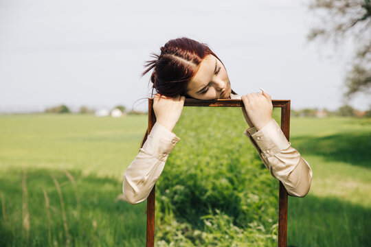 Sad girl holding mirror with reflection of grass at field