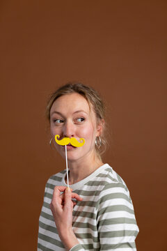 Thoughtful blond woman with mustache prop against brown background