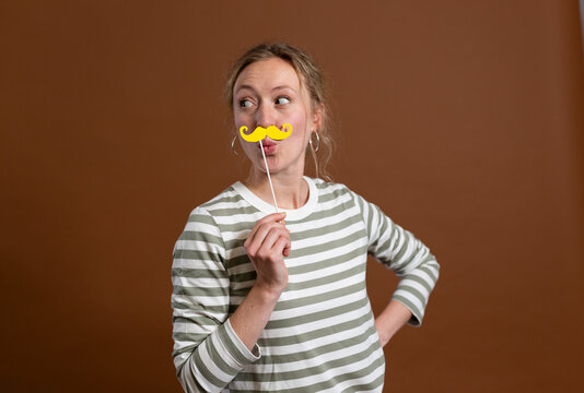 Woman with hand on hip holding mustache prop in studio