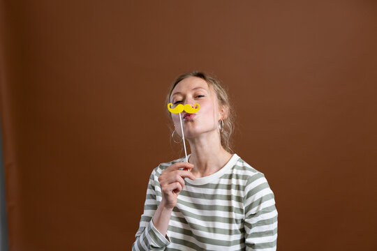 Woman holding mustache prop and puckering over brown background