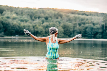 Cold water swimming for elderly woman. Senior sporty woman standing in lake during cold winter...