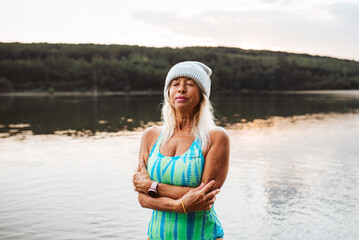 Cold water swimming for elderly woman. Senior sporty woman standing in lake during cold winter...