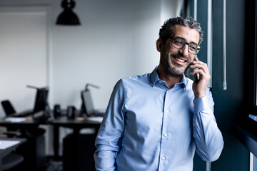 Happy businessman talking on smart phone in office
